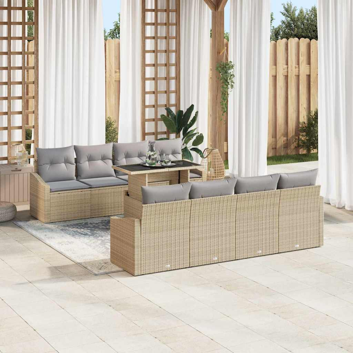 Terrassenset im Freien mit beigefarbenen Korbsesseln, grauen Kissen, einem Tisch und weißen Vorhängen. Im Hintergrund ein Holzzaun und Grün.