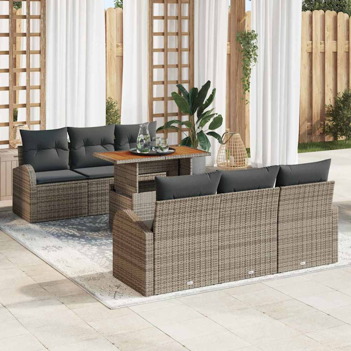 Terrassenmöbel-Set mit gewebten grauen Möbeln, dunklen Kissen, Holztisch, Teppich und weißen Vorhängen.