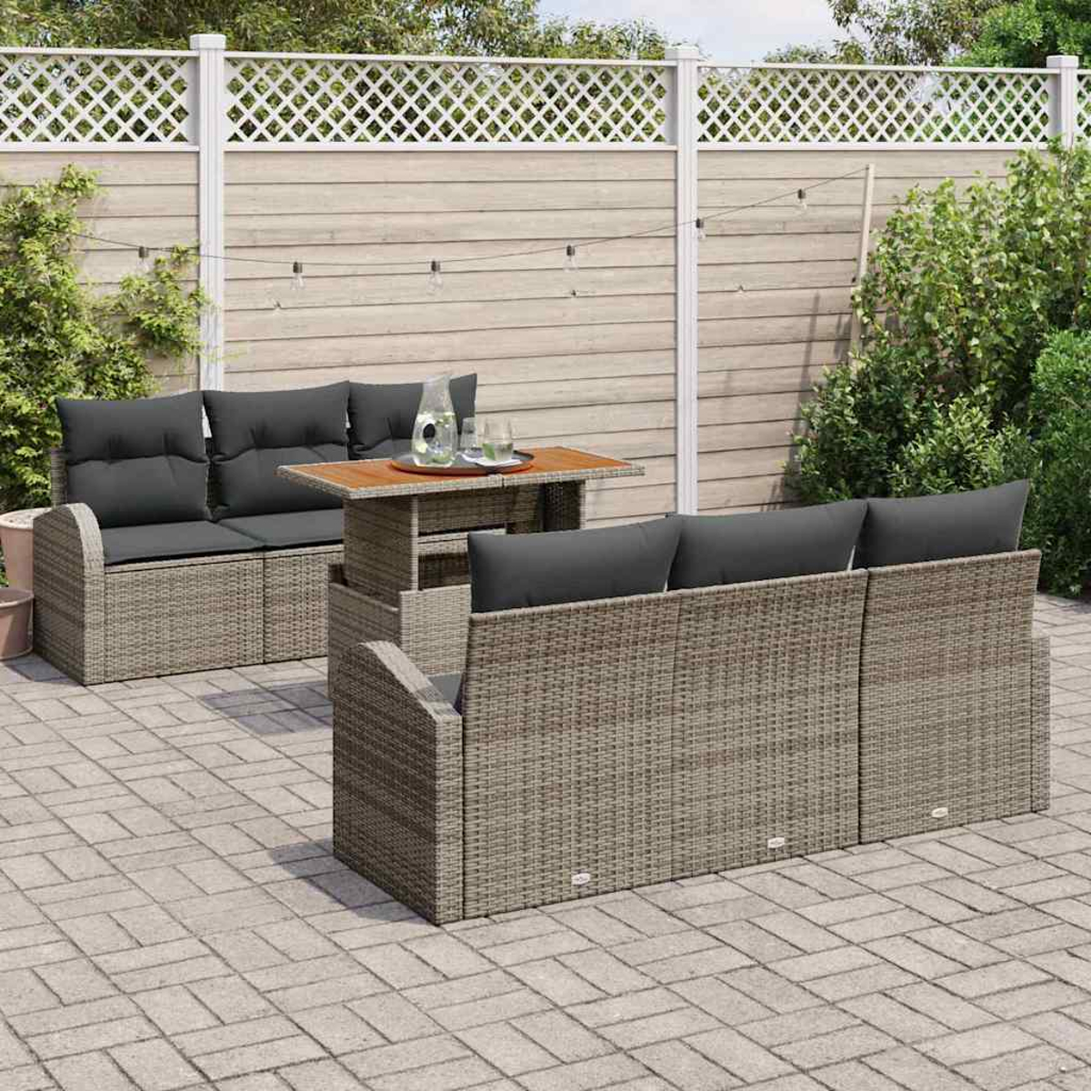 Terrassengarnitur im Freien mit grauen Kissen. Ein Tisch mit Getränken steht zwischen zwei Sofas. Ein weißer Zaun und Grün im Hintergrund.