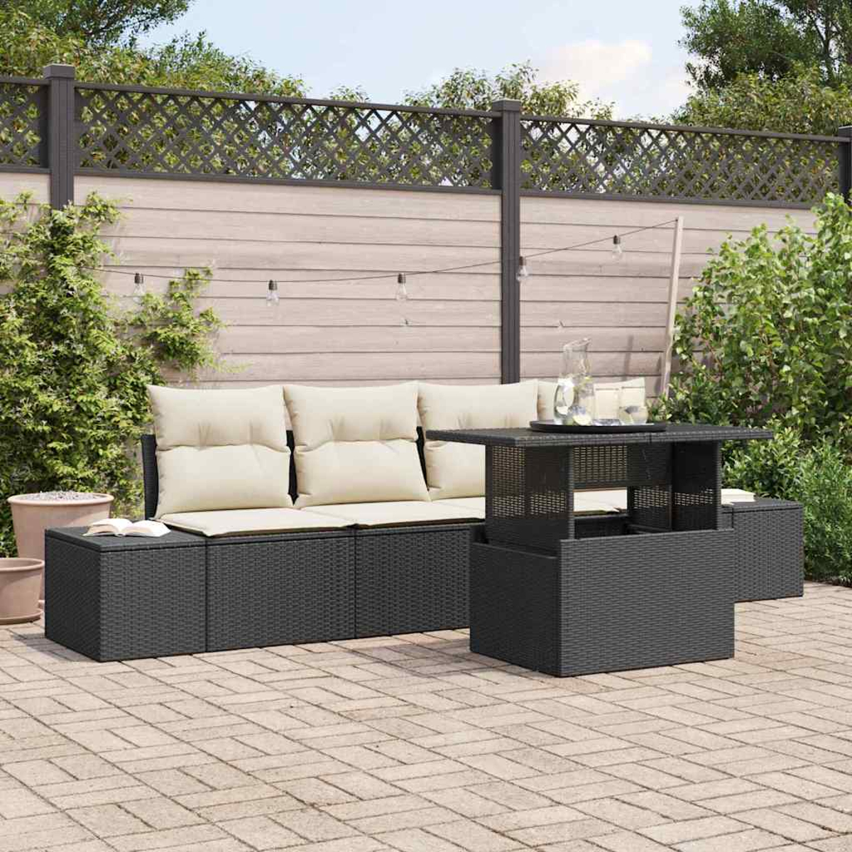 Garten-Sitzgruppe mit schwarzen Korbmöbeln und beigen Kissen. Ein Tisch mit Glas und ein Zaun im Hintergrund.