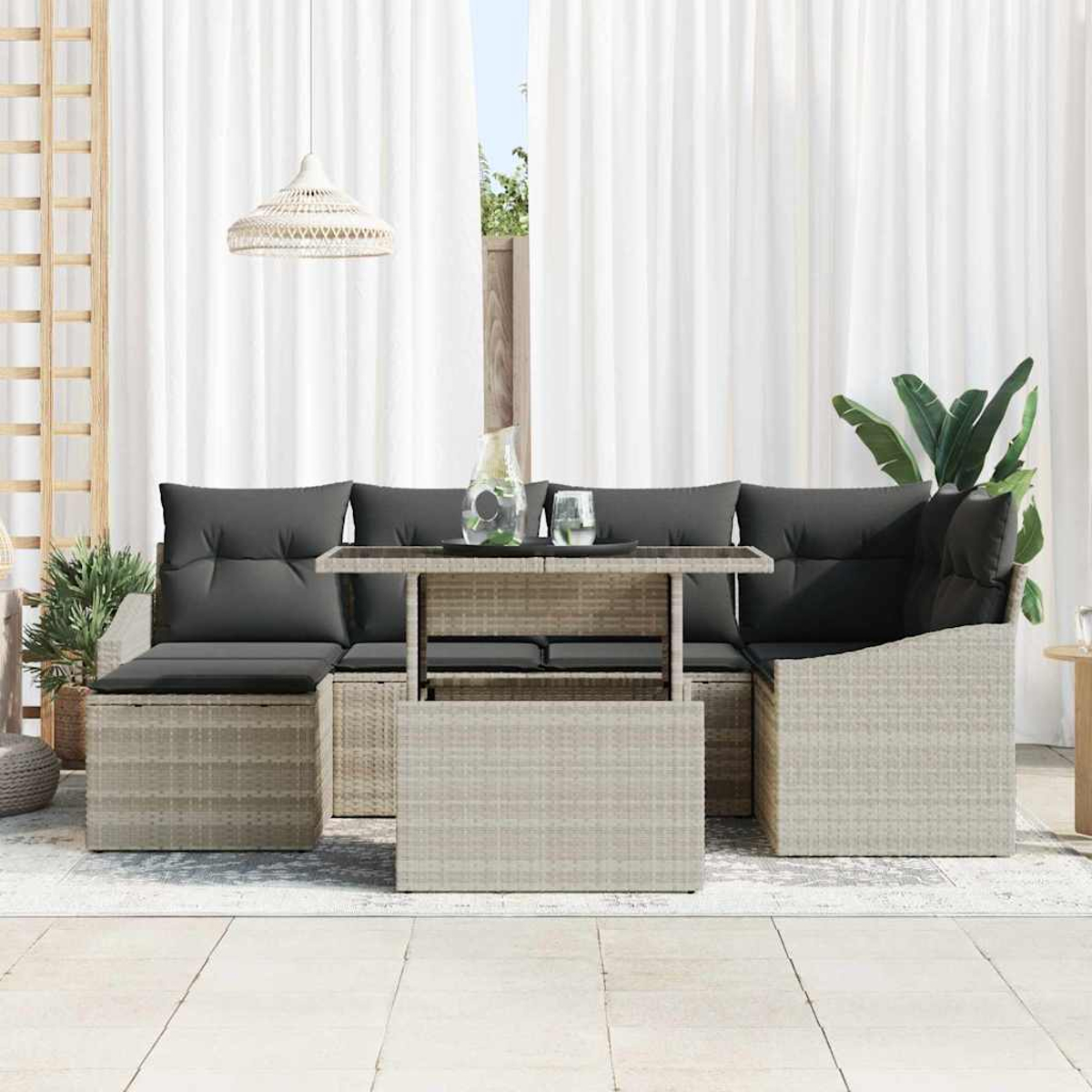 Geflochtenes Gartenmöbel-Set mit grauen Kissen und einem Tisch. Weiße Vorhänge und eine Hängelampe im Hintergrund.