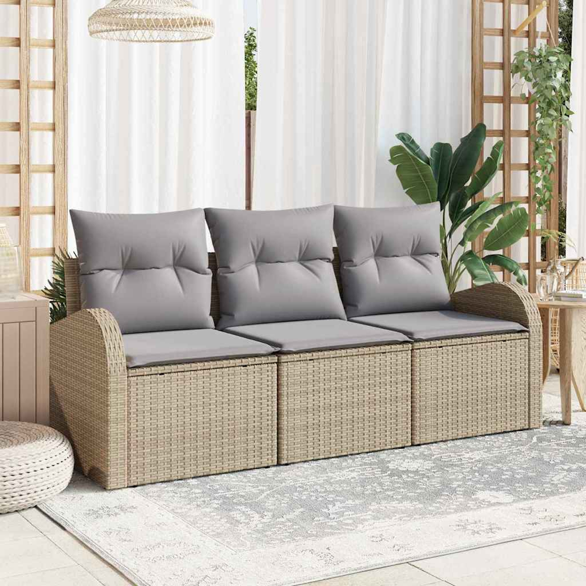 Ein Korbbettsofa mit grauen Kissen steht auf einem gemusterten Teppich. Dahinter sind weiße Vorhänge und Pflanzen zu sehen.