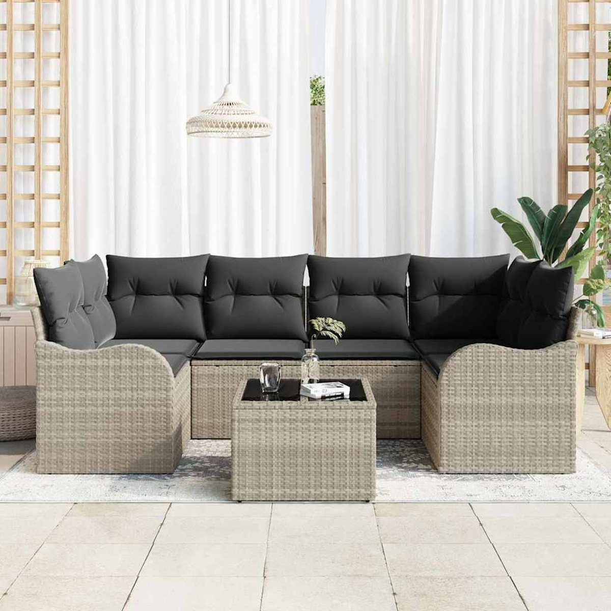 Geflochtenes Outdoor-Ecksofa mit grauen Kissen und einem kleinen Tisch. Weiße Vorhänge im Hintergrund, mit einer Hängelampe.