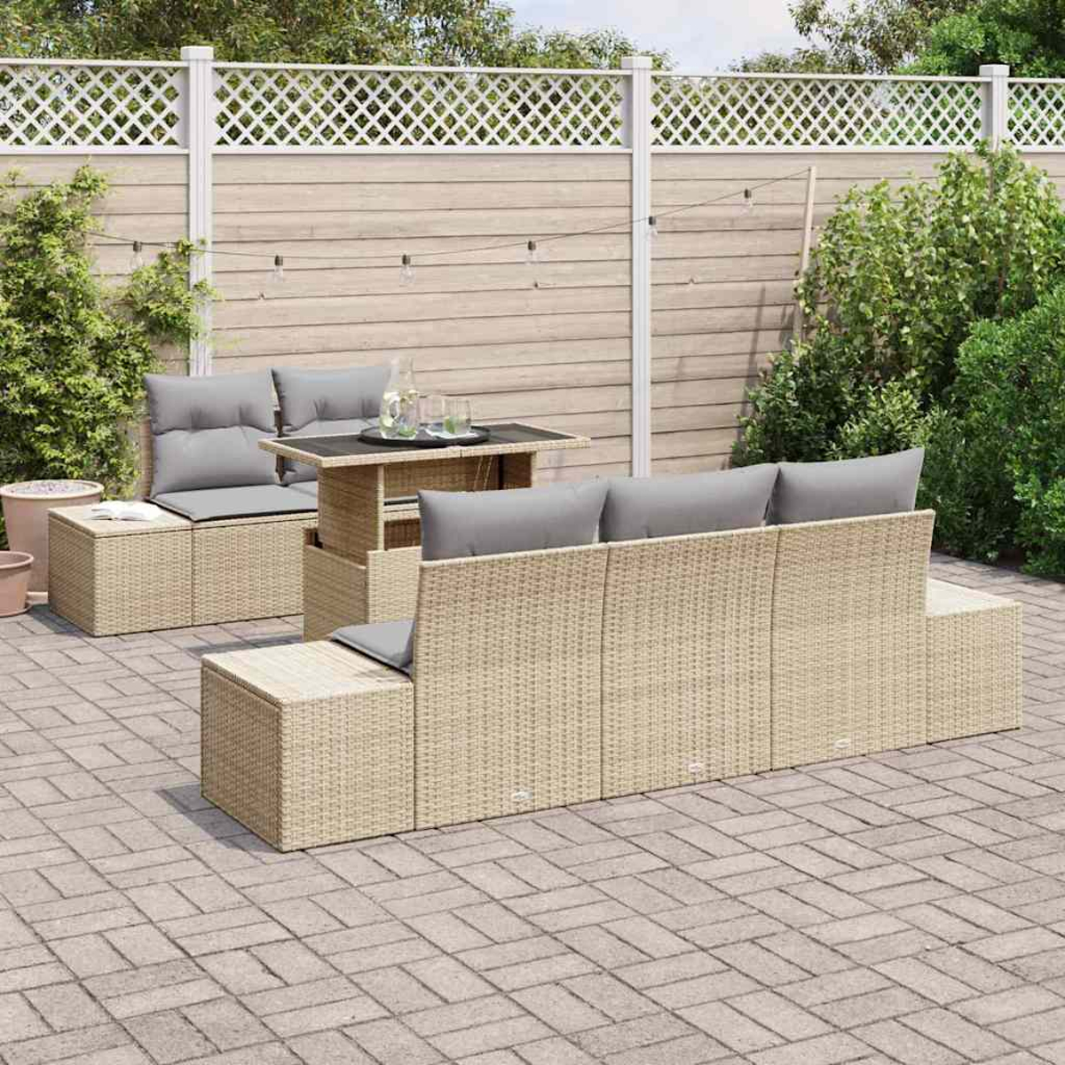 Garten-Set mit beigefarbenen Möbeln, grauen Kissen und kleinem Tisch. Weißer Zaun und Grün im Hintergrund.