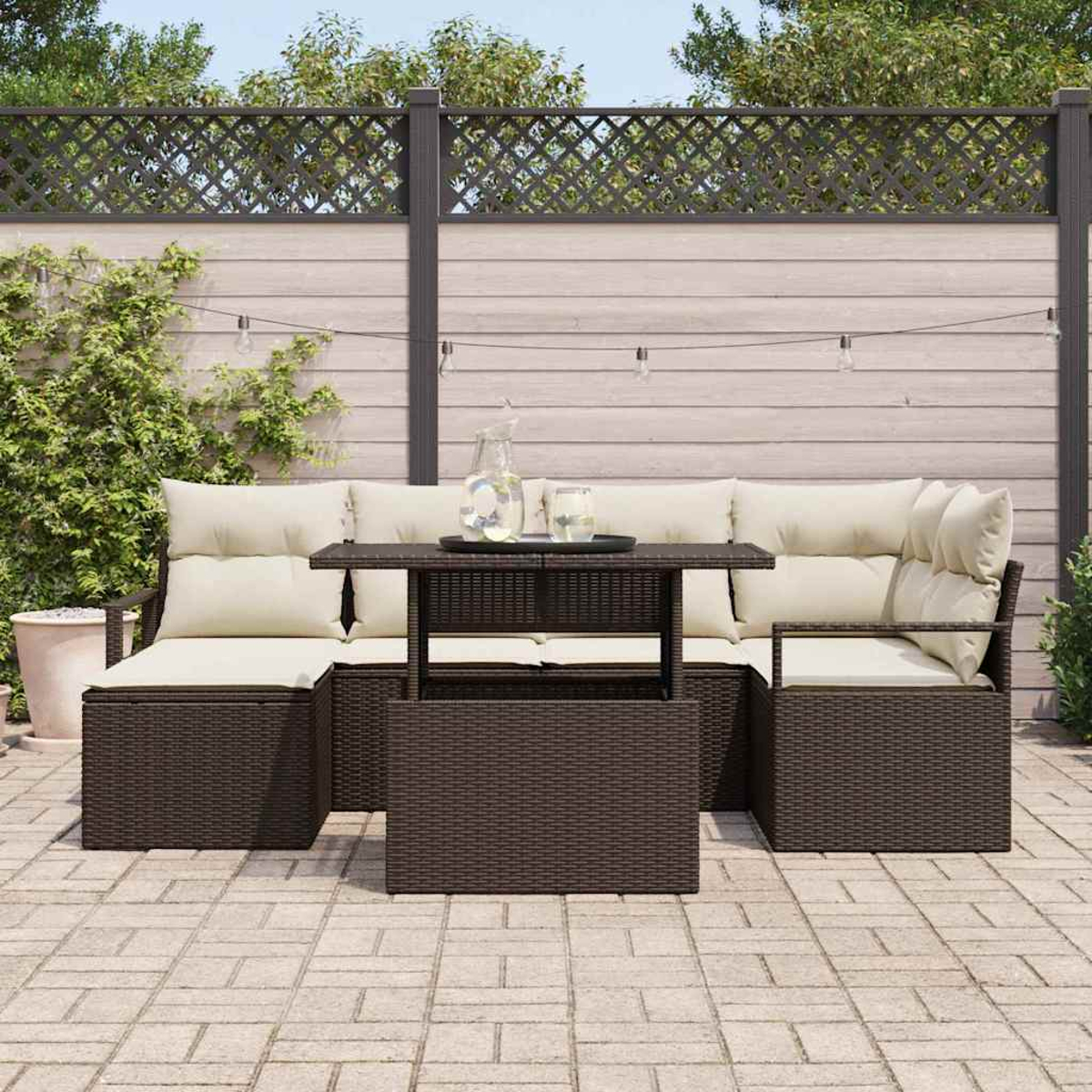 Garten-Set mit braunen Korbmöbeln, beigefarbenen Kissen und einem Tisch mit Hubfunktion. Im Hintergrund ein Holzzaun und Pflanzen.