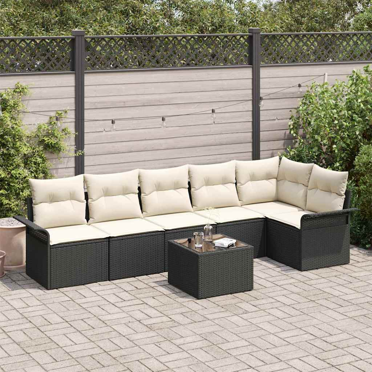 L-förmiges Outdoor-Sofa mit cremefarbenen Kissen und einem kleinen Tisch auf einer gepflasterten Terrasse. Im Hintergrund ein Holzzaun und Pflanzen.