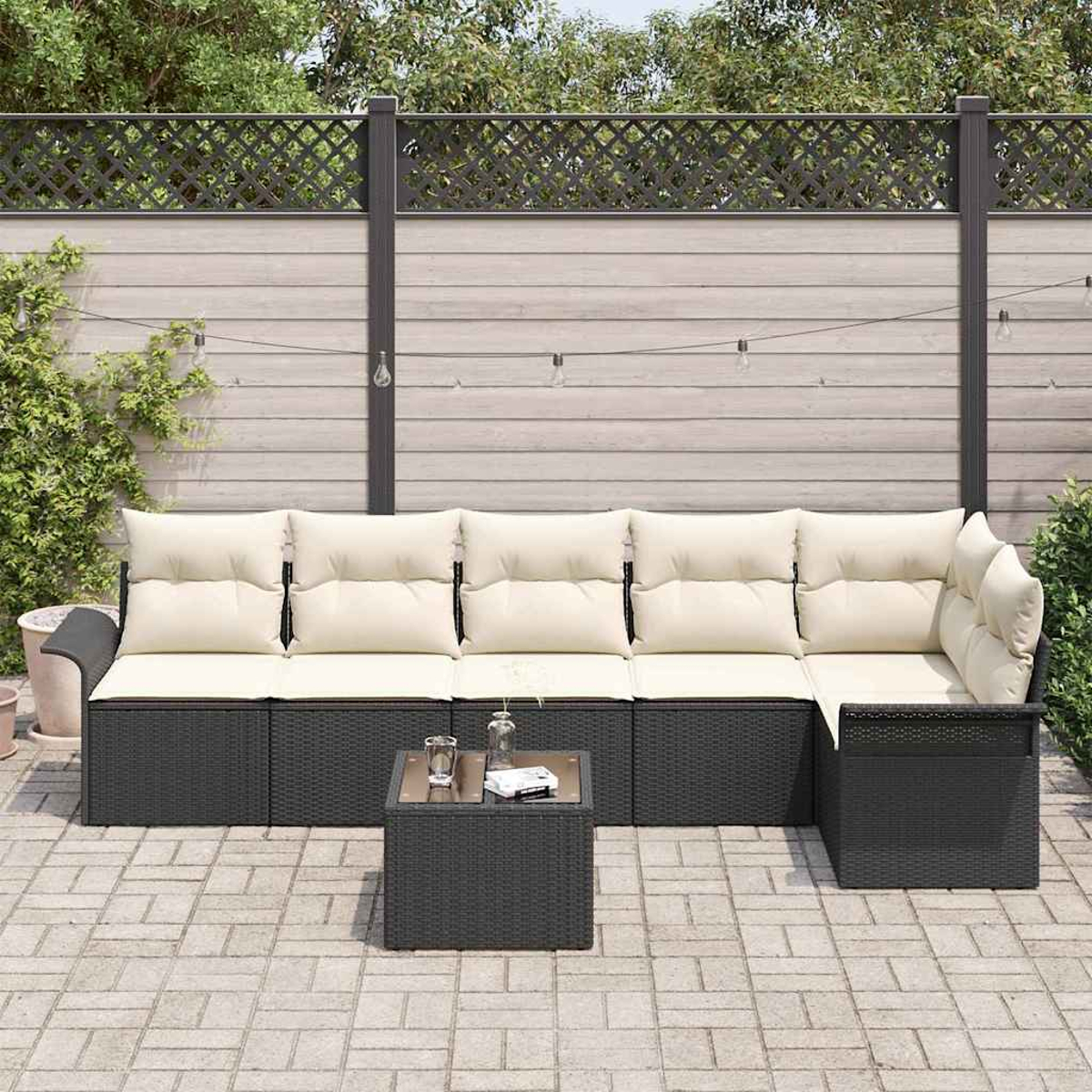 Garten-Terrassenset mit dunklen Möbeln, beigen Kissen und einem kleinen Tisch. Im Hintergrund ein Holzzaun und Pflanzen.