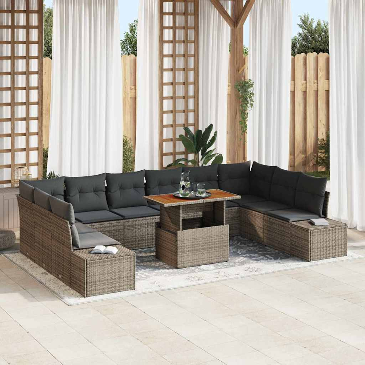 Zona de estar al aire libre con muebles de ratán, cojines grises y una mesa de madera. Cortinas blancas y celosía de madera al fondo.