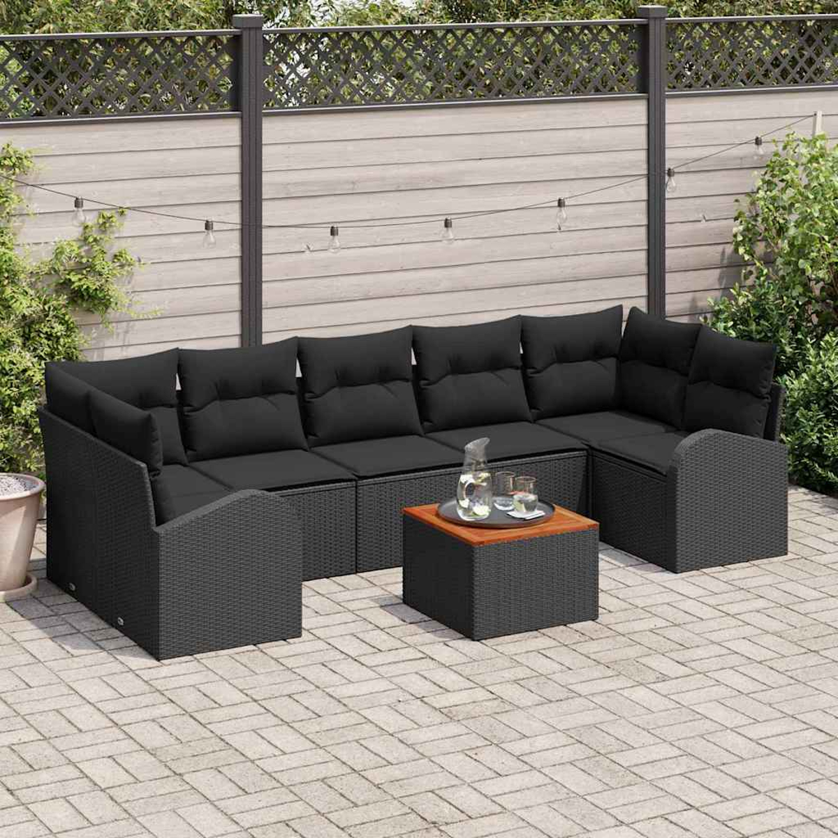 Schwarzes Outdoor-Rattan-Ecksofa mit schwarzen Kissen und einem Holztisch. Auf einer Terrasse mit Zaun und Pflanzen im Hintergrund.