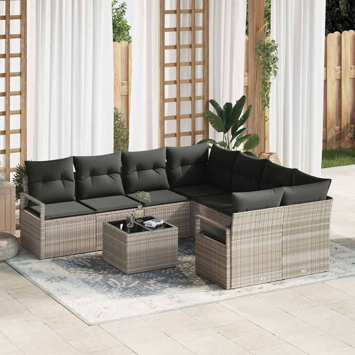 Outdoor-Ecksofa mit grauen Kissen, einem kleinen Tisch und einem Teppich. Weiße Vorhänge und Holzzaun im Hintergrund.