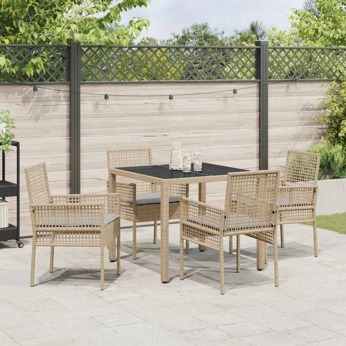 Terrassenset im Freien mit quadratischem Tisch, vier Stühlen und einem dekorativen Zaun im Hintergrund. Auf dem Tisch stehen Gläser und eine Kanne.