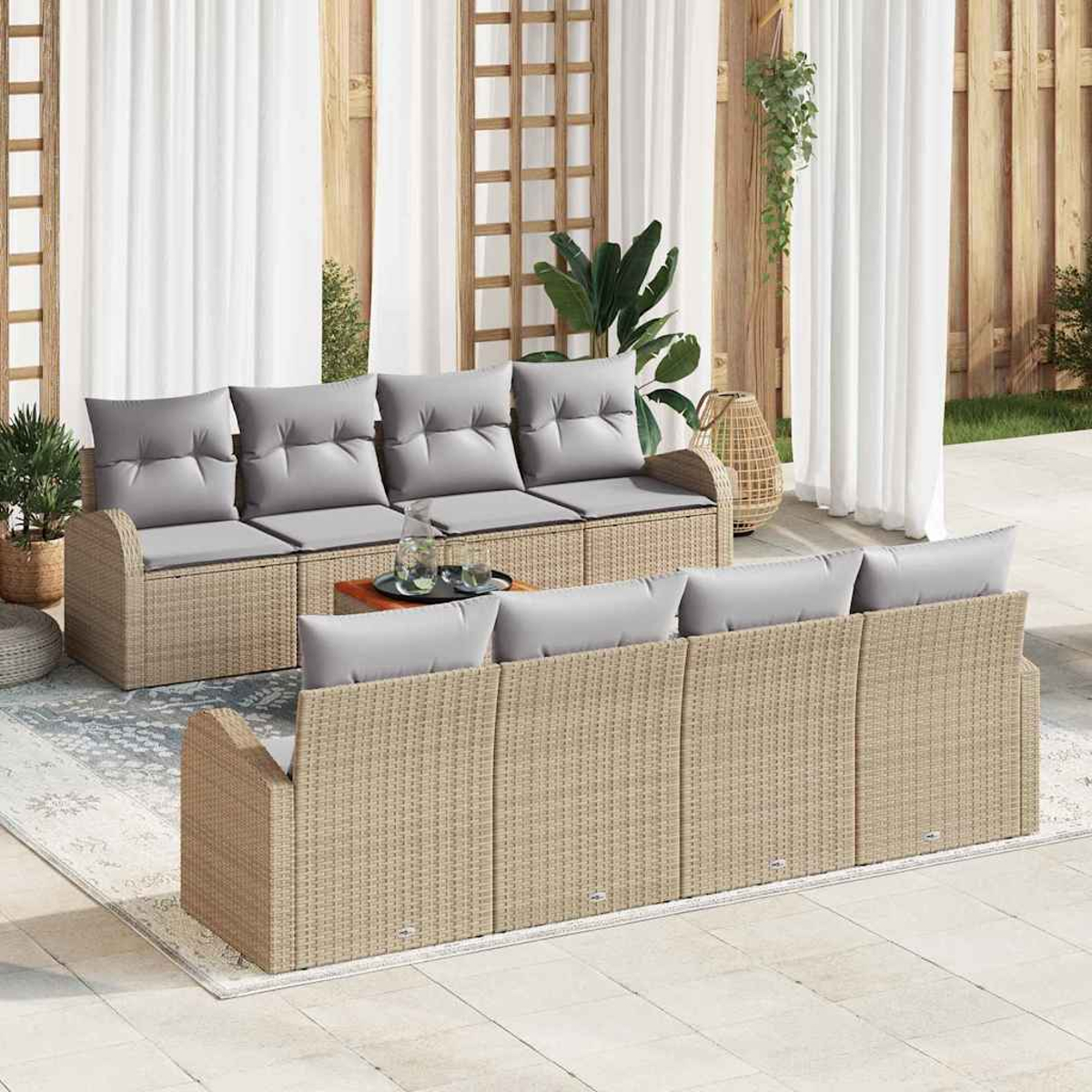 Outdoor-Sitzbereich mit geflochtenen Sofas, grauen Kissen, Holztisch, Pflanzen, weißen Vorhängen und einem gemusterten Teppich.