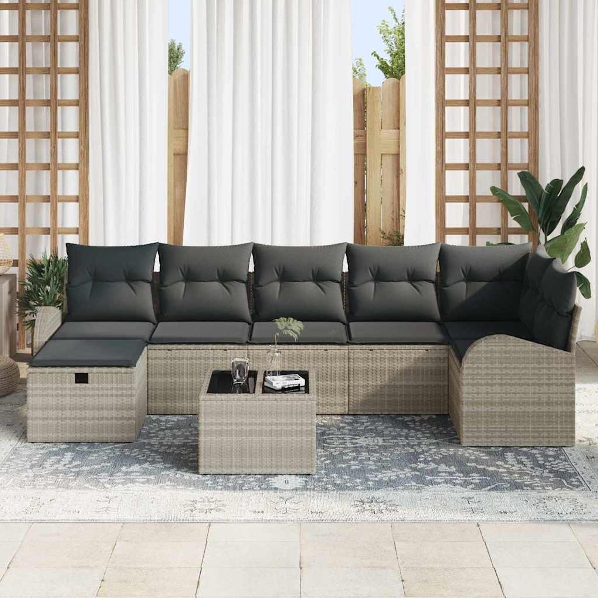 Outdoor-Sitzgruppe mit grauen Kissen. Enthält Ecksofa, Ottoman und quadratischen Couchtisch auf einem gemusterten Teppich.