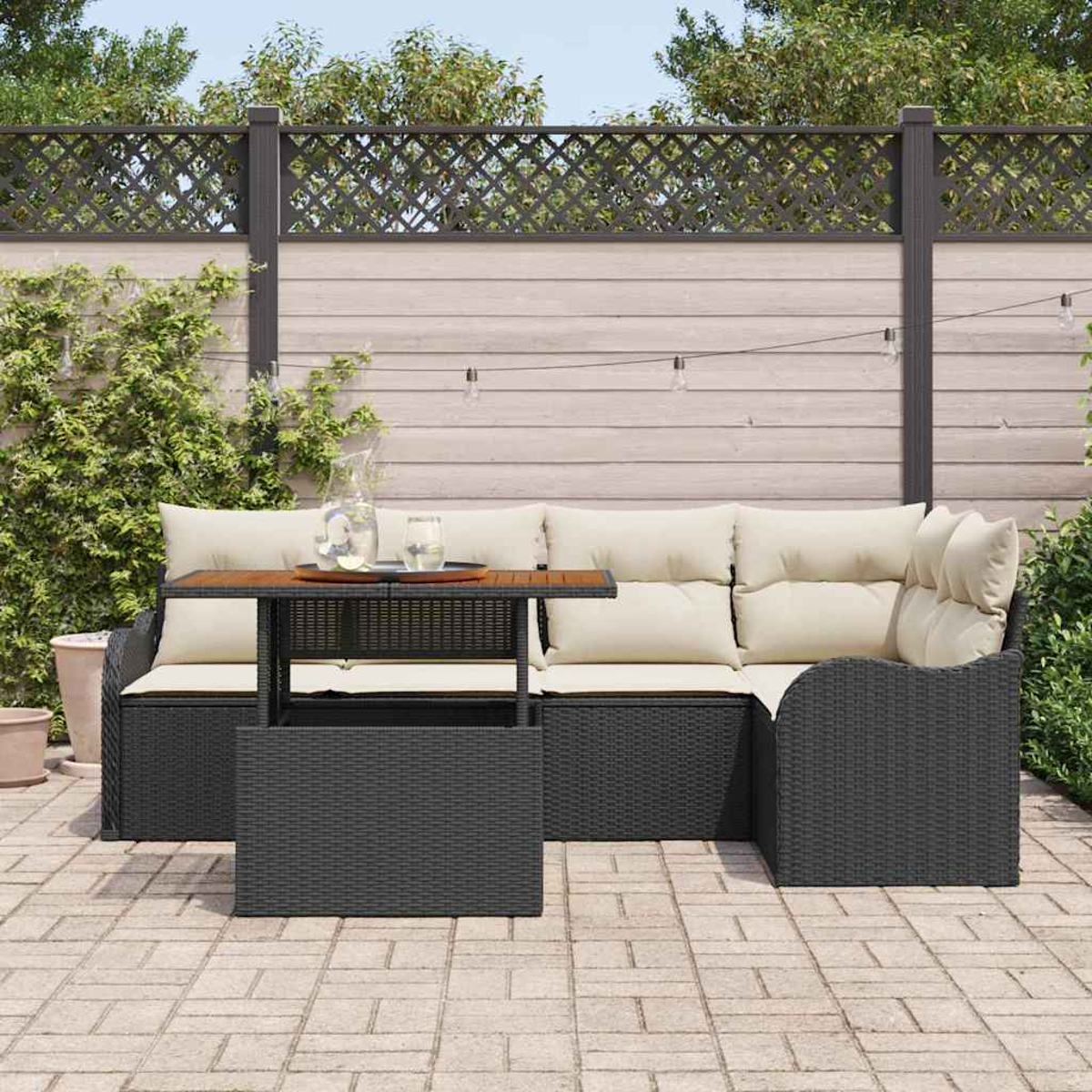 Garten-Set: dunkles Korbmöbel mit cremefarbenen Kissen, Holztisch und dekorativem Zaun in einem Hinterhof.