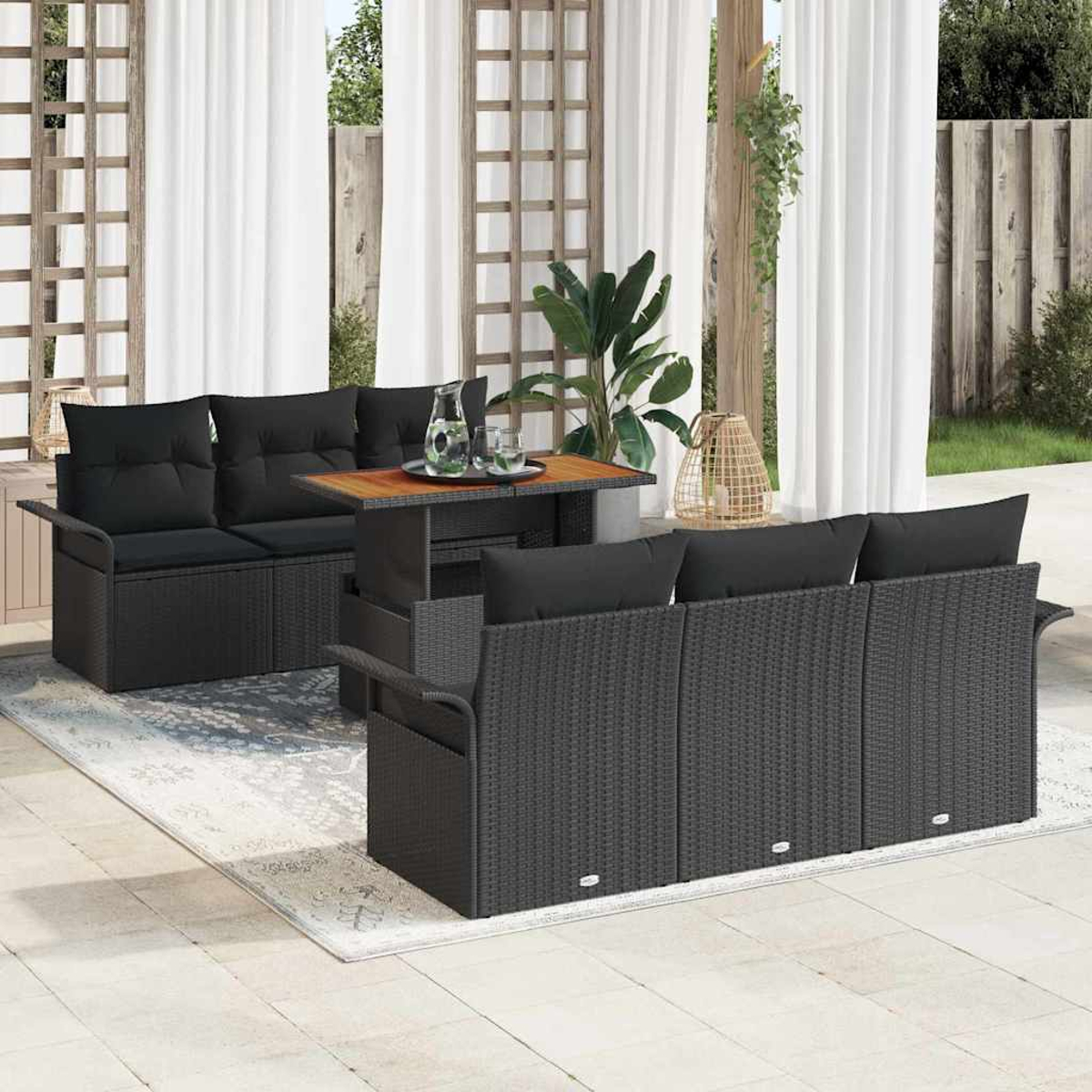 Gartenmöbel-Set: schwarze Korbsessel mit schwarzen Kissen, ein Tisch und ein Teppich. Transparente weiße Vorhänge und Pflanzen im Hintergrund.