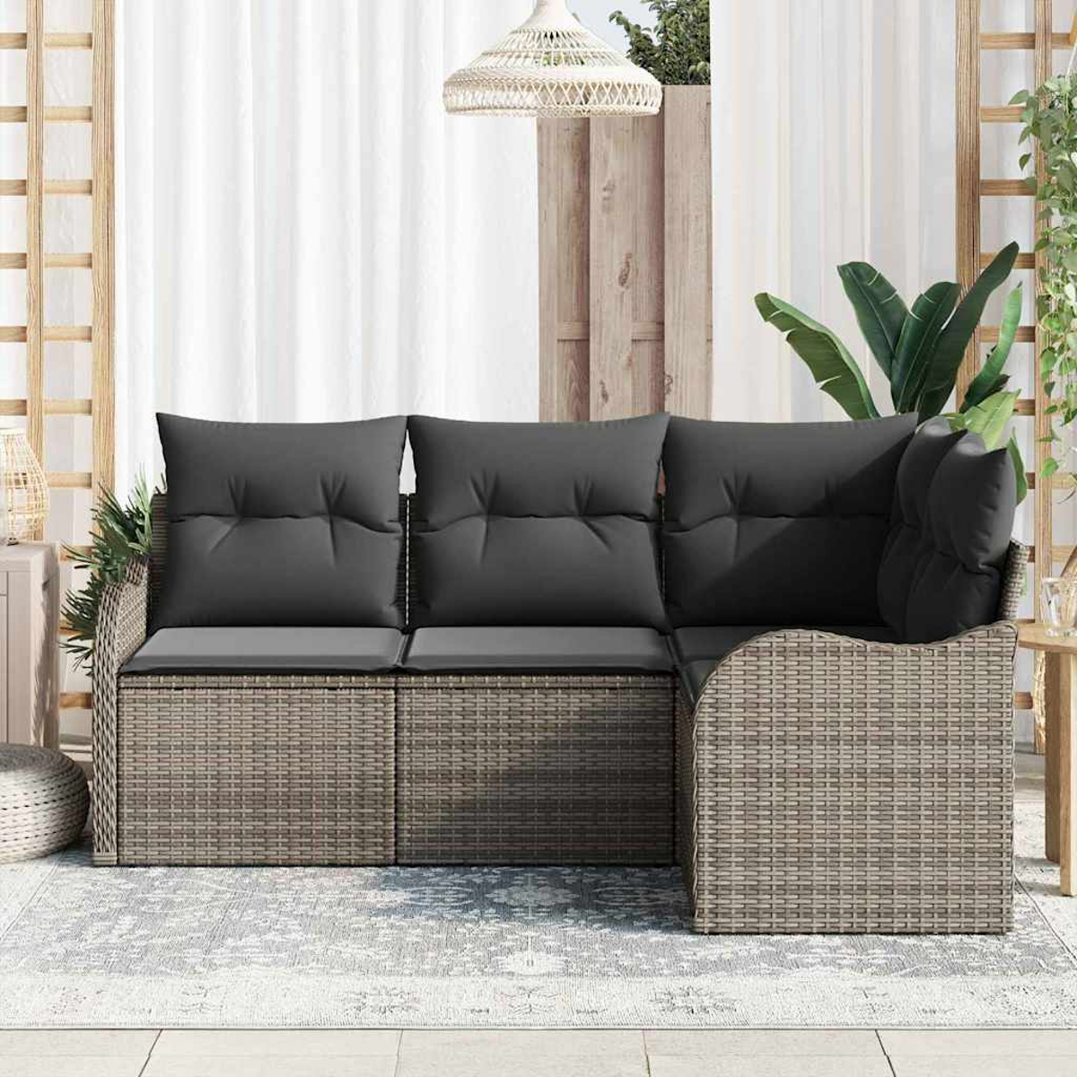 Ein Ecksofa für den Außenbereich mit grauen Kissen. Im Hintergrund ein weißer Vorhang und Pflanzen. Ein geflochtenes Licht hängt oben.
