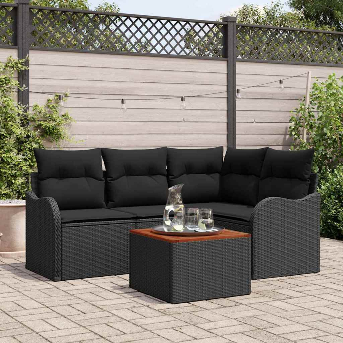 Schwarze Outdoor-Wicker-Möbel mit schwarzen Kissen, einem Couchtisch mit Holzplatte, Glaskrug und Gläsern.