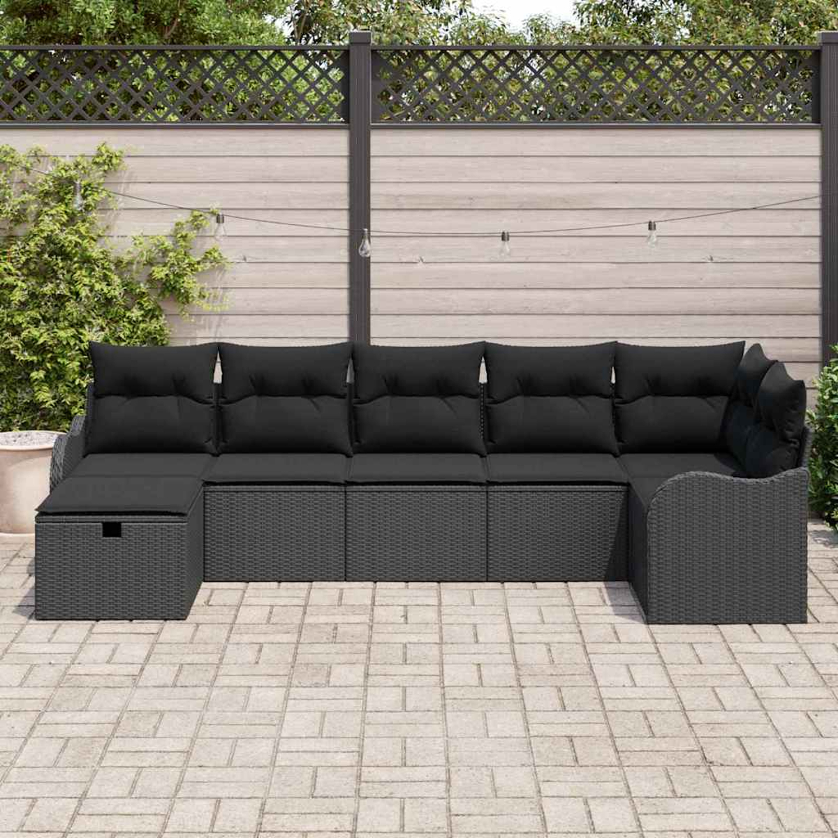 Sofá seccional exterior con cojines negros. El sofá está en un patio de ladrillos con una valla de madera al fondo.