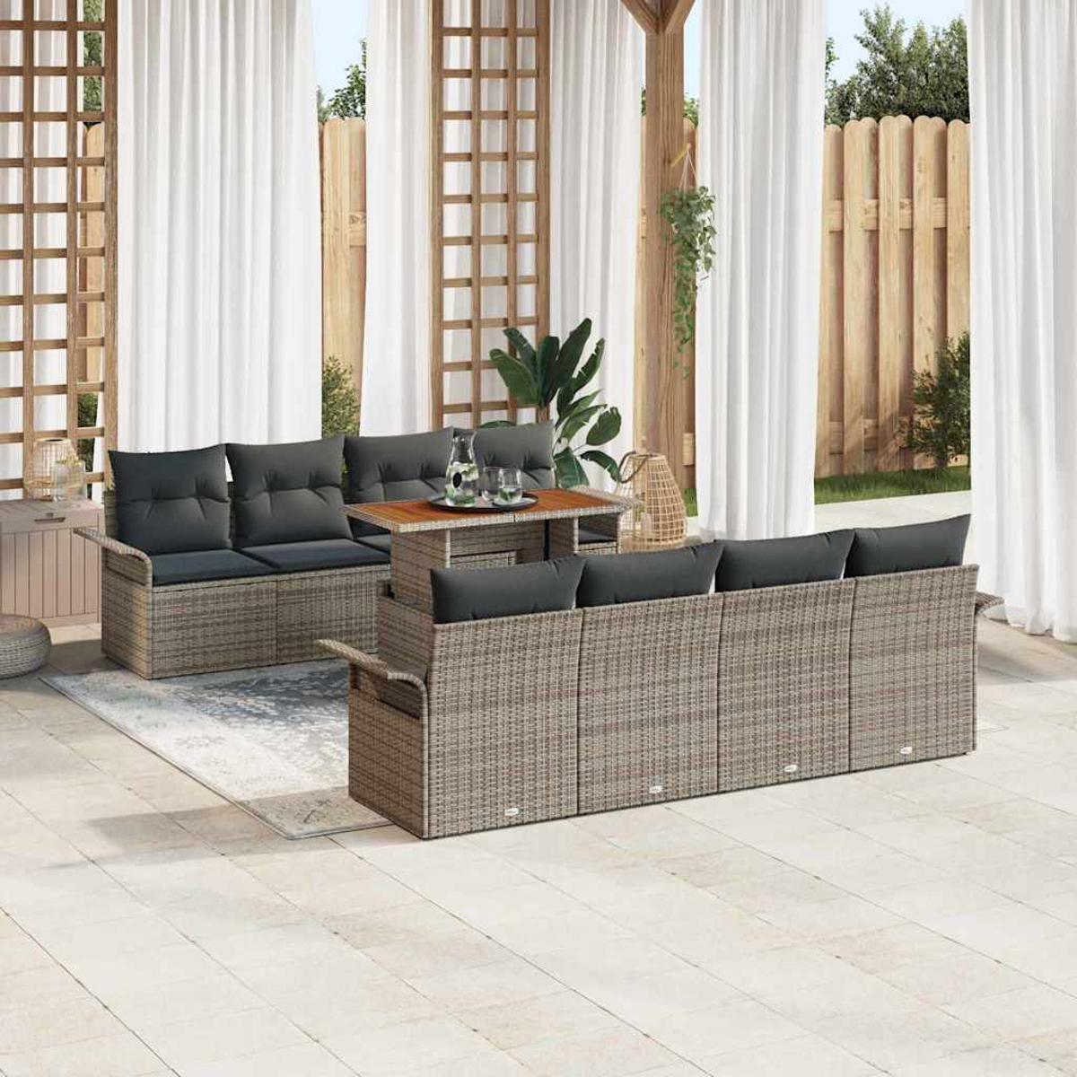 Terrassen-Set mit Rattansofas, Kissen und Tisch. Weiße Vorhänge und Holzzaun im Hintergrund.