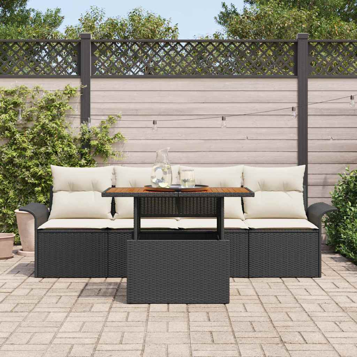 Garten-Terrassenset mit schwarzem gewebtem Sofa, Holztisch und cremefarbenen Kissen. Eine klare Kanne und Gläser stehen auf dem Tisch.