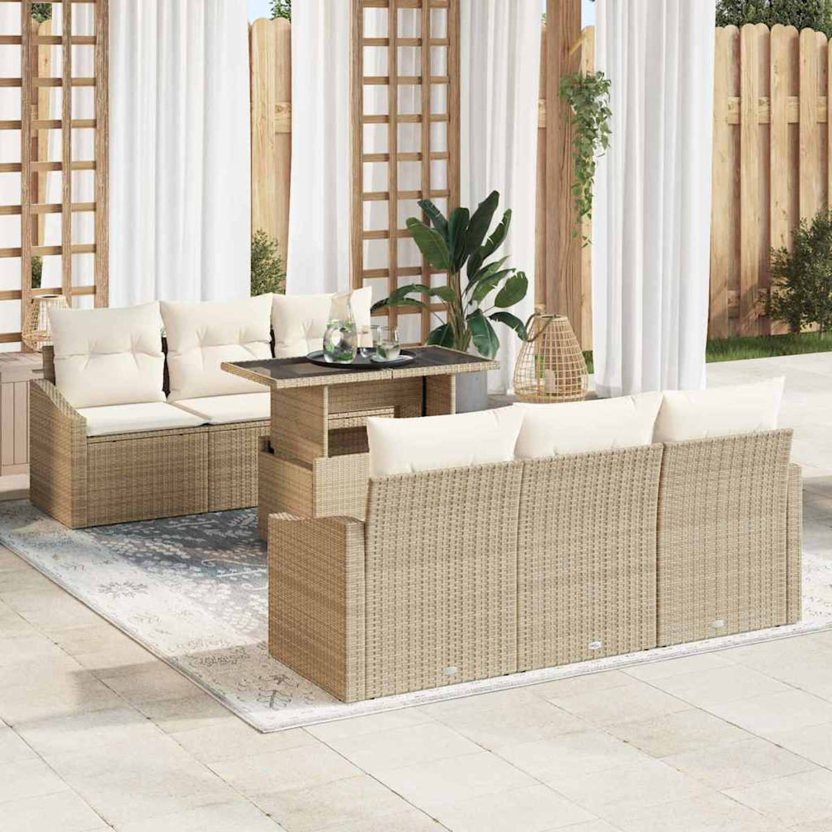 Terrassenset im Freien mit beigen Korbmöbeln, cremefarbenen Kissen, einem Tisch und weißen Vorhängen. Ein Teppich liegt auf dem Boden.