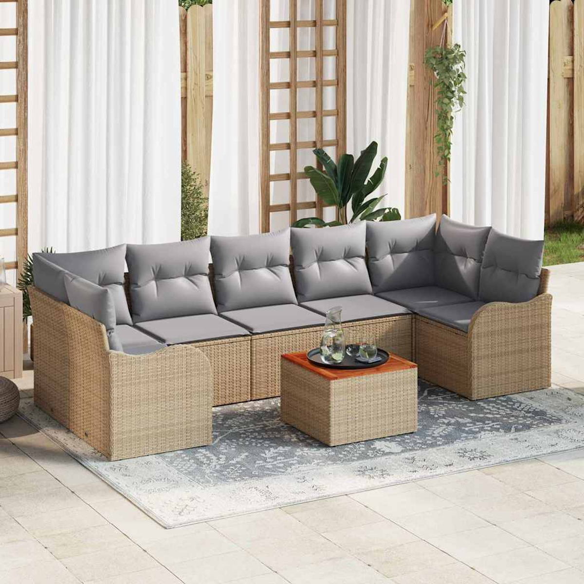 Gartensofa mit grauen Kissen und Rattangestell, Couchtisch, Teppich. Weiße Vorhänge und Holzgitter im Hintergrund.