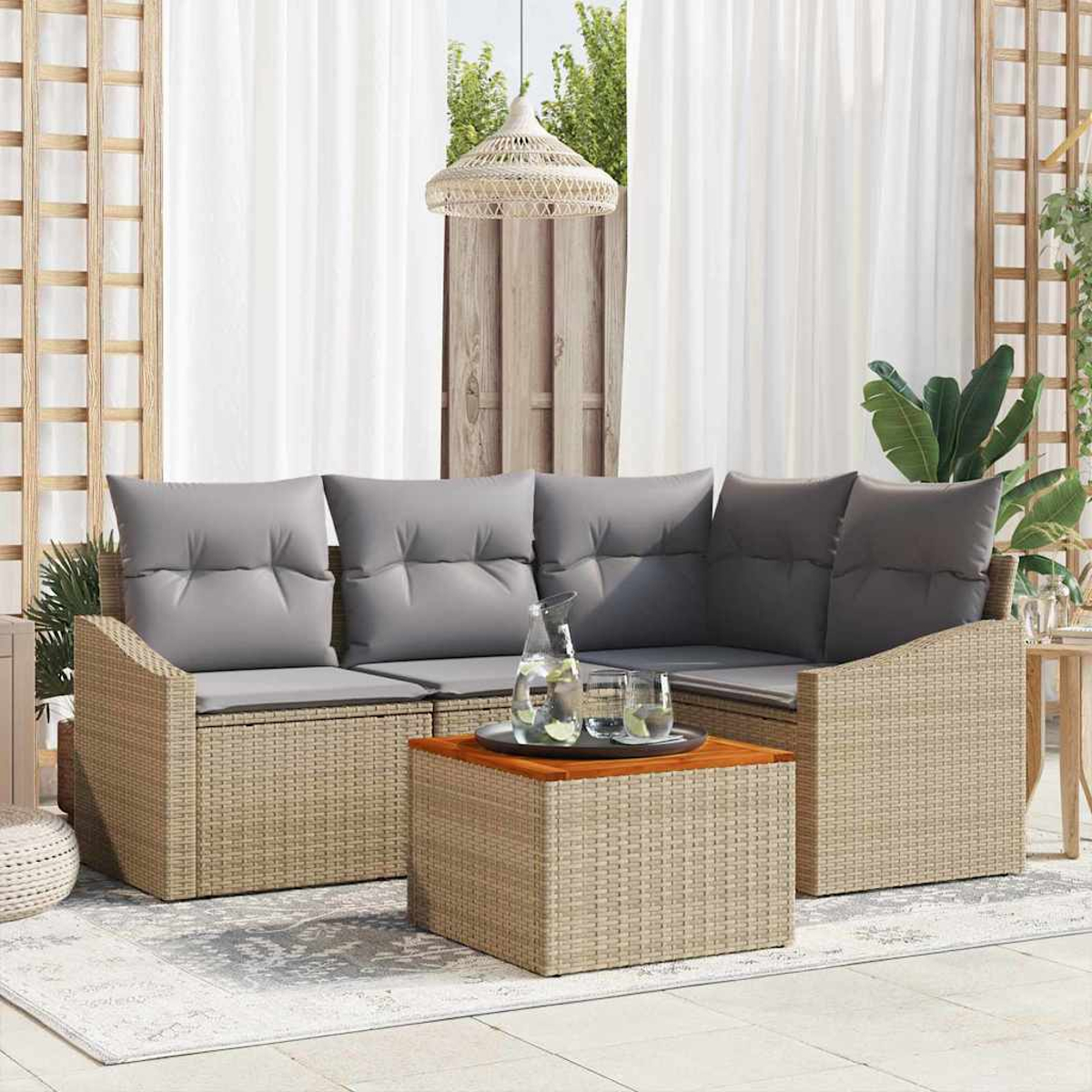 Outdoor-Sitzgruppe mit grauen Kissen, Couchtisch mit Getränken und weißen Vorhängen. Korbmöbel auf einer Terrasse.