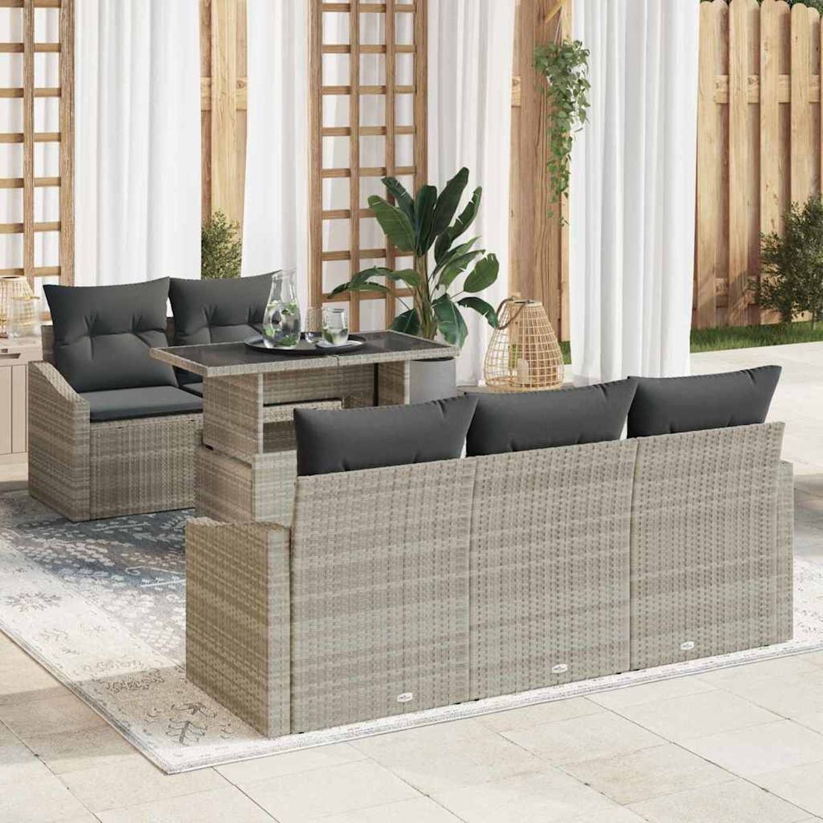 Outdoor-Rattan-Möbel-Set, bestehend aus Sofa, Stühlen und Tisch. Im Hintergrund Pflanzen, Holzzaun und weiße Vorhänge.