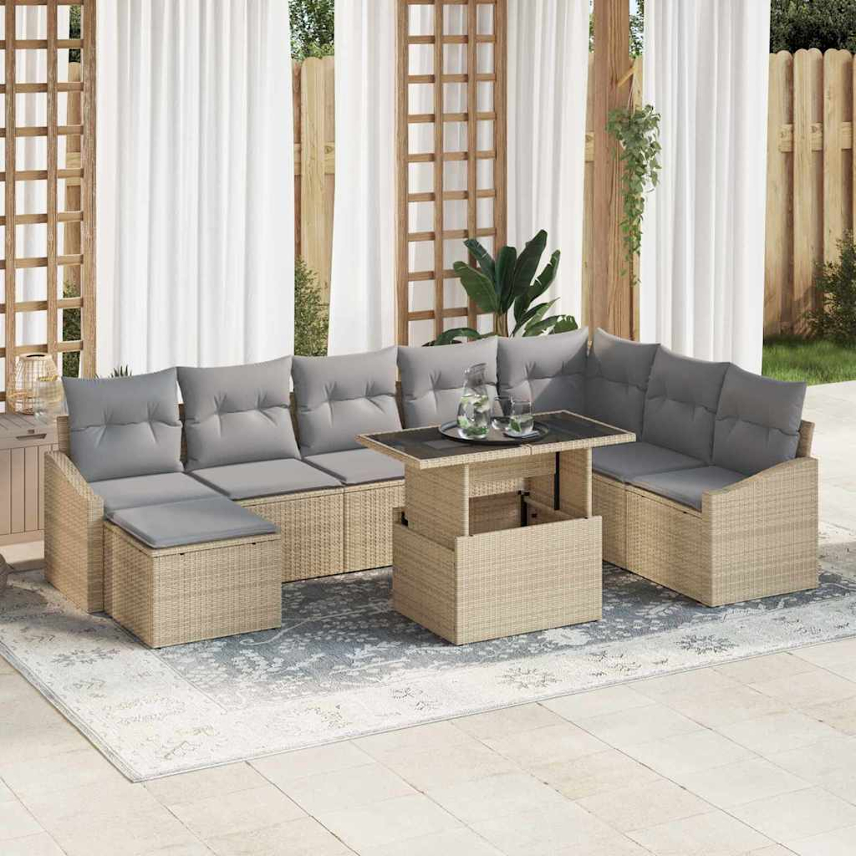 Outdoor-Sitzgruppe aus Korbgeflecht mit grauen Kissen und einem Tisch mit Hebevorrichtung. Weiße Vorhänge und Holzgitter im Hintergrund, alles auf einer Terrasse.