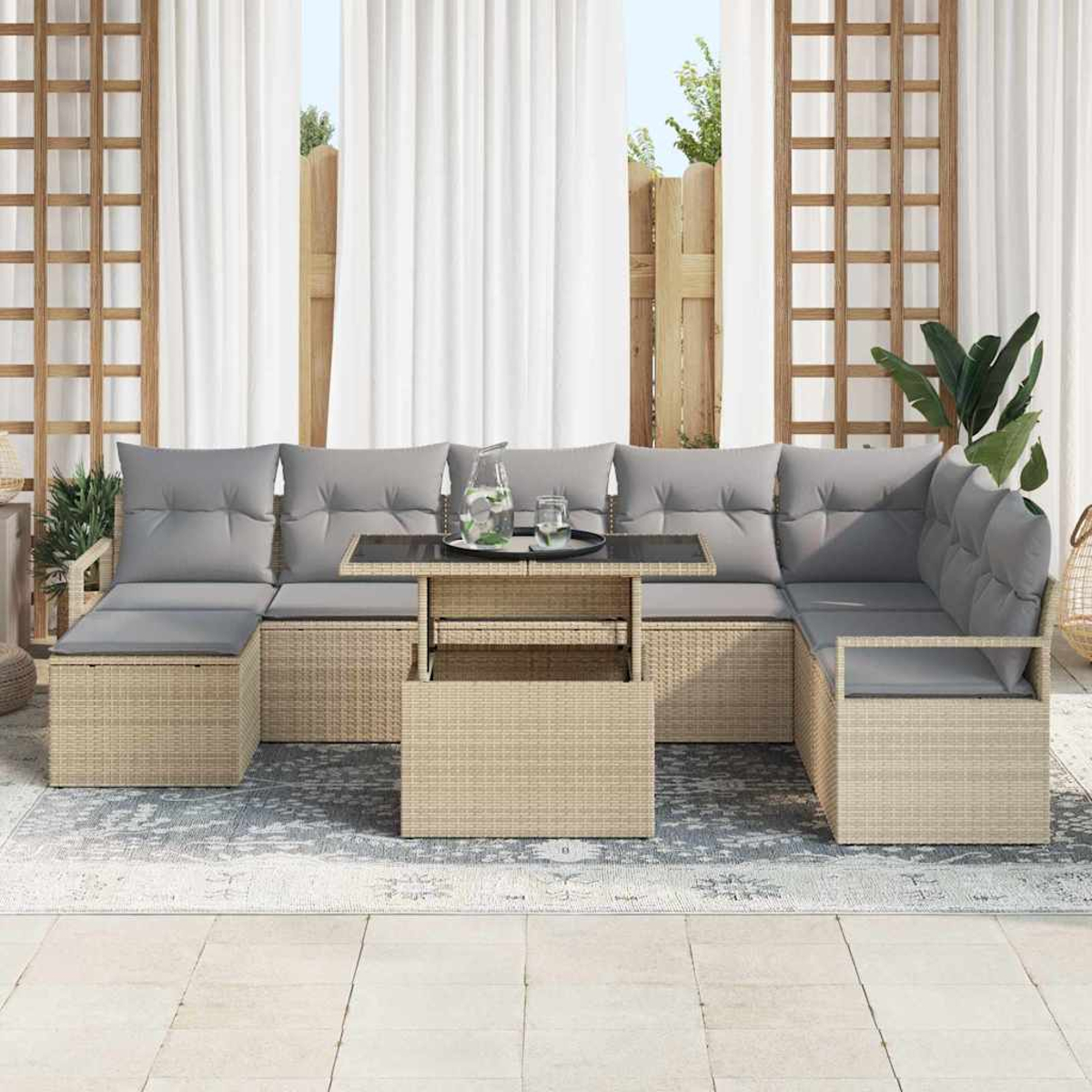 Geflochtenes Outdoor-Ecksofa mit grauen Kissen und Tisch. Im Hintergrund Vorhänge, Holzgitter und ein Zaun. Pflanzen sind sichtbar.