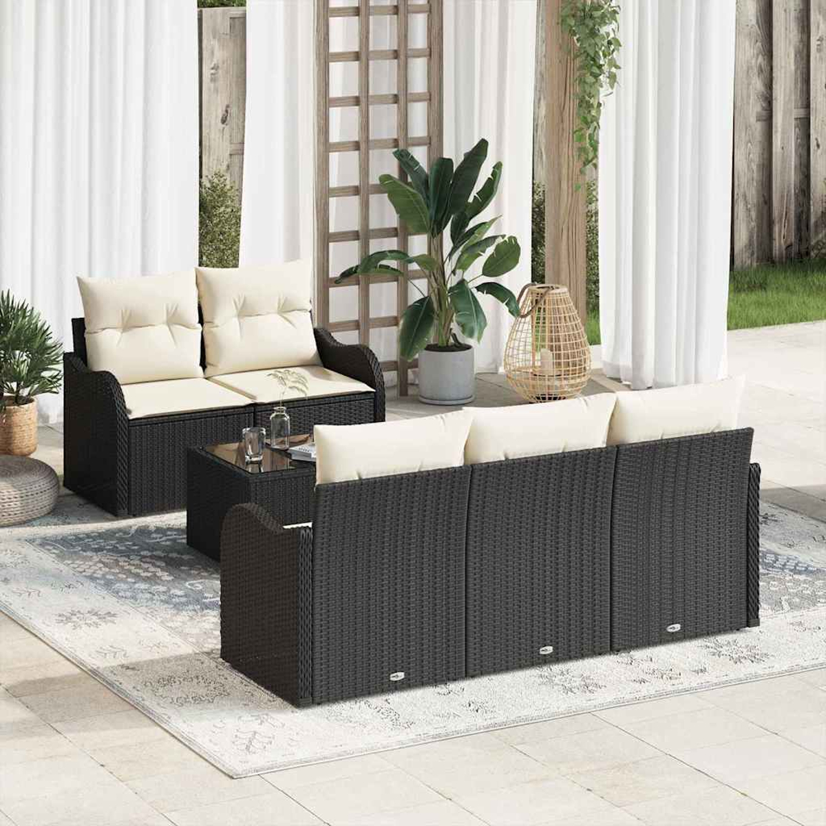 Gartenmöbel-Set auf einem Teppich. Es umfasst eine Doppelsitzerbank, ein Dreisitzer-Sofa und einen kleinen Tisch. Pflanzen und Vorhänge sind im Hintergrund.