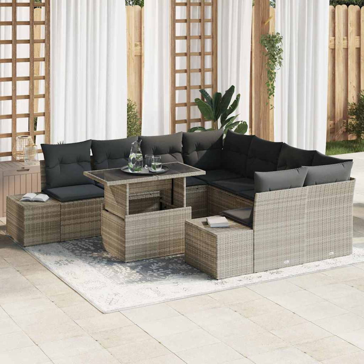 Gartencouch mit dunklen Kissen, Glastisch, Teppich und weißen Vorhängen. Hintergrund mit Holzstruktur und Pflanzen.