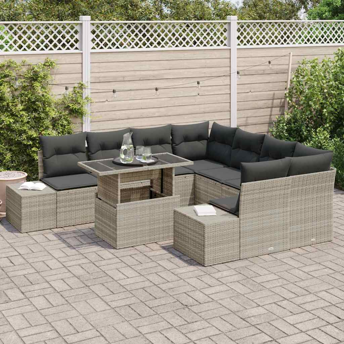 Garten-Sitzgruppe mit grauen Kissen, einem Tisch mit Getränken, auf einer Steinterrasse, hinter einem Zaun und Grün.