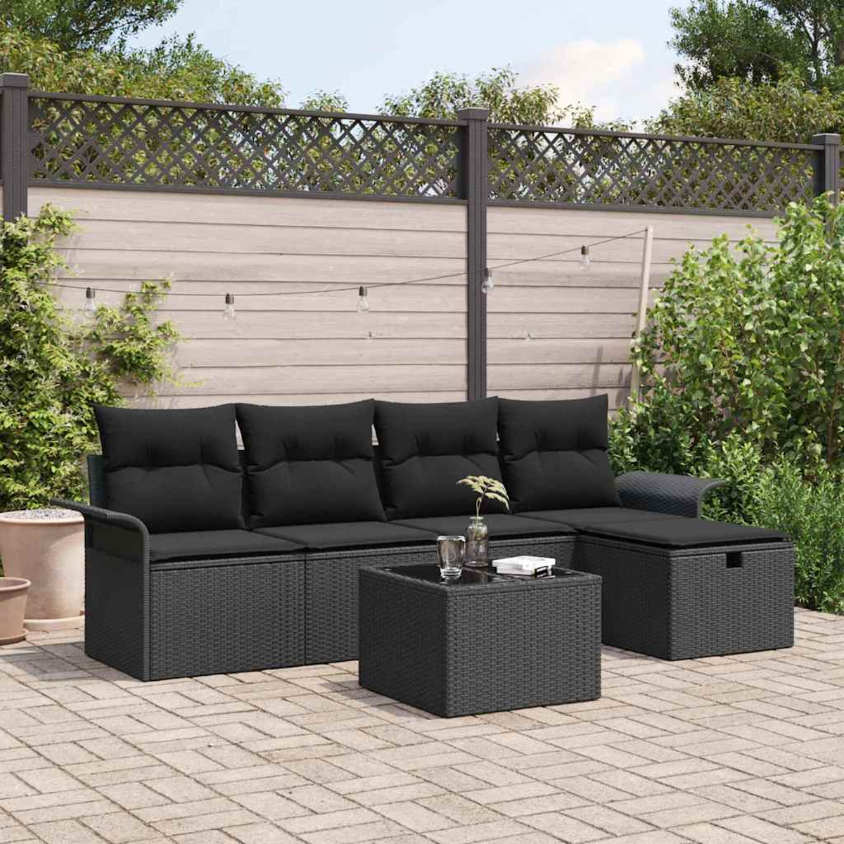 Ein schwarzes Outdoor-Sofa aus Korbgeflecht mit Kissen, ein quadratischer Tisch und eine Bank. Dahinter ein Holzzaun und Grün.