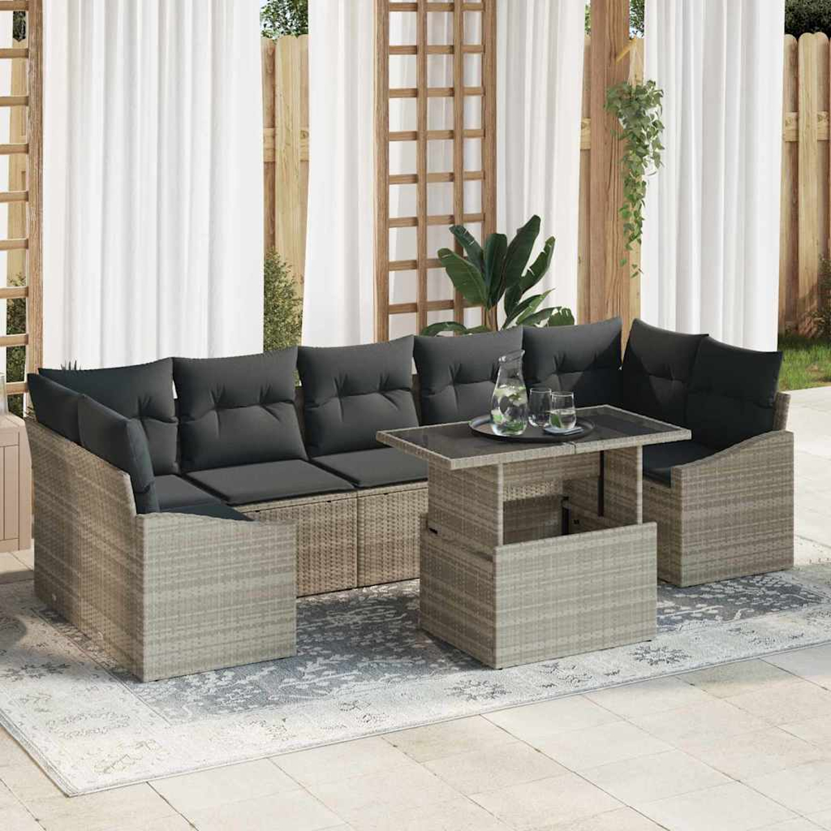 Garten-Sitzgruppe mit grauen Kissen und einem Tisch. Weiße Vorhänge und Holzgitter im Hintergrund. Karaffe und Gläser auf dem Tisch.