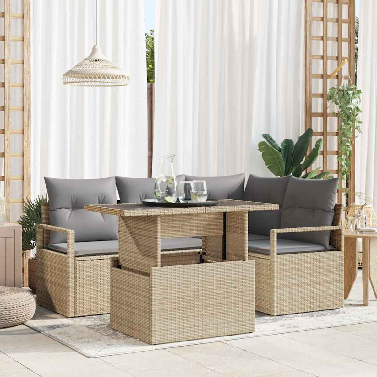 Escena al aire libre con muebles tejidos, mesa con bebidas, cojines grises, cortinas blancas y lámpara colgante.