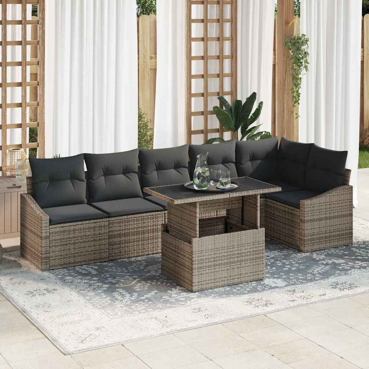 Garten-Sitzgruppe: Korbmöbel-Sofa mit grauen Kissen, Tisch mit Gläsern und Krug, auf gemustertem Teppich und weißen Vorhängen.