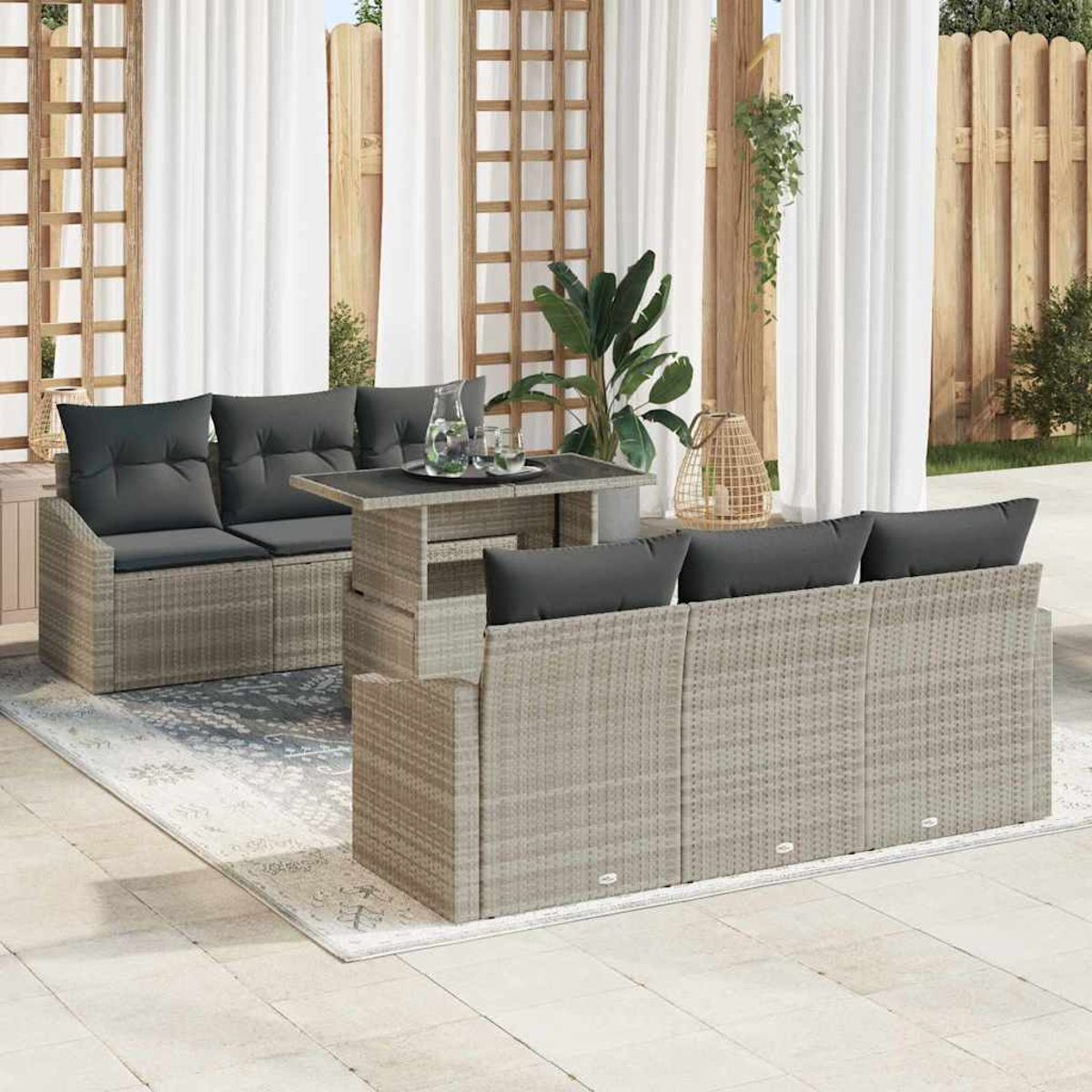 Juego de muebles de exterior: sofás de mimbre grises, mesa y alfombra. Cojines negros, cortinas blancas y celosía de madera al fondo.
