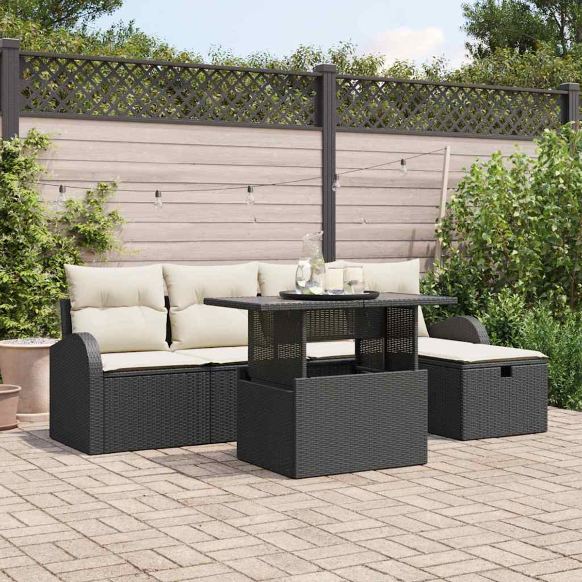 Terrassenset mit schwarzer Korbmöbeln und beigen Kissen. Enthält ein Sofa, einen Tisch und eine Stauraum-Ottomane auf einer Ziegelterrasse.