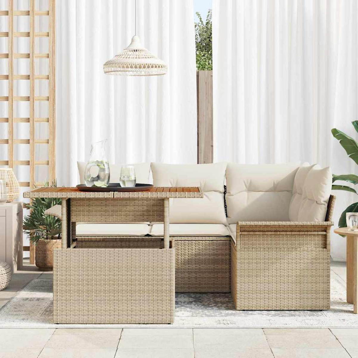 Terrassenset mit gewebtem Tisch, cremefarbenen Kissen und weißen Vorhängen. Krug und Gläser stehen auf dem Tisch.