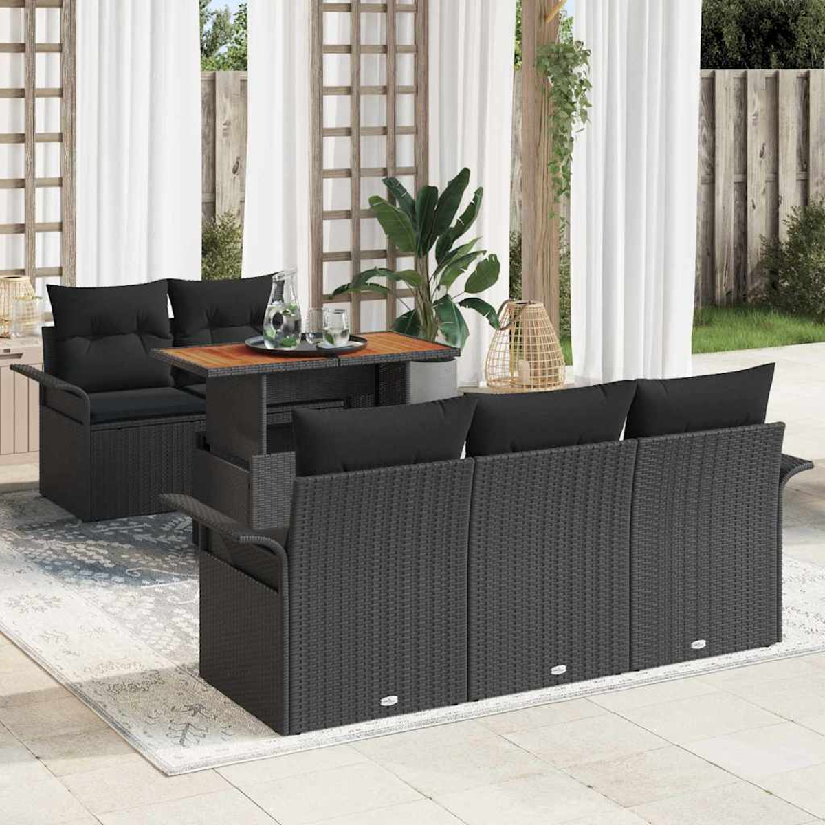 Garten-Terrassenset mit schwarzen Korbmöbeln, Kissen und einem Holztisch. Weiße Vorhänge und Pflanzen im Hintergrund.