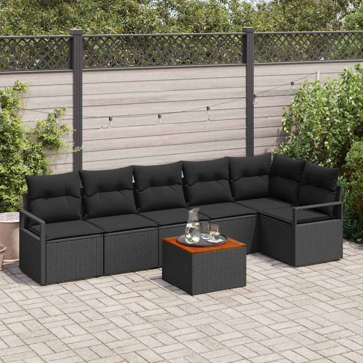 Juego de muebles de patio: sofá seccional de ratán negro con cojines y una mesita. Sobre un patio de ladrillos con valla de madera.