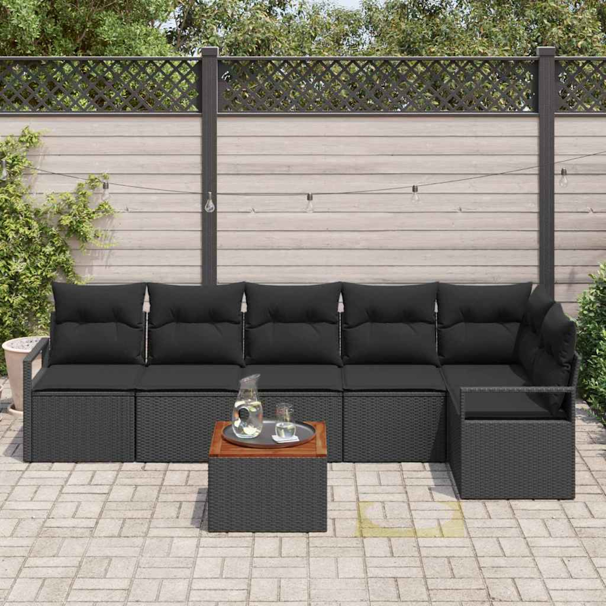 Mobiliario de exterior: un sofá seccional gris con cojines negros, una mesita con una bandeja y una valla de madera al fondo.