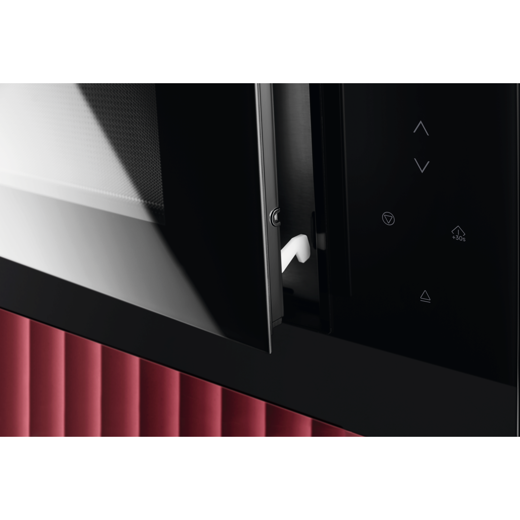 Primer plano de un horno microondas. La puerta está ligeramente abierta con un asa blanca. Debajo, una pared roja texturizada.