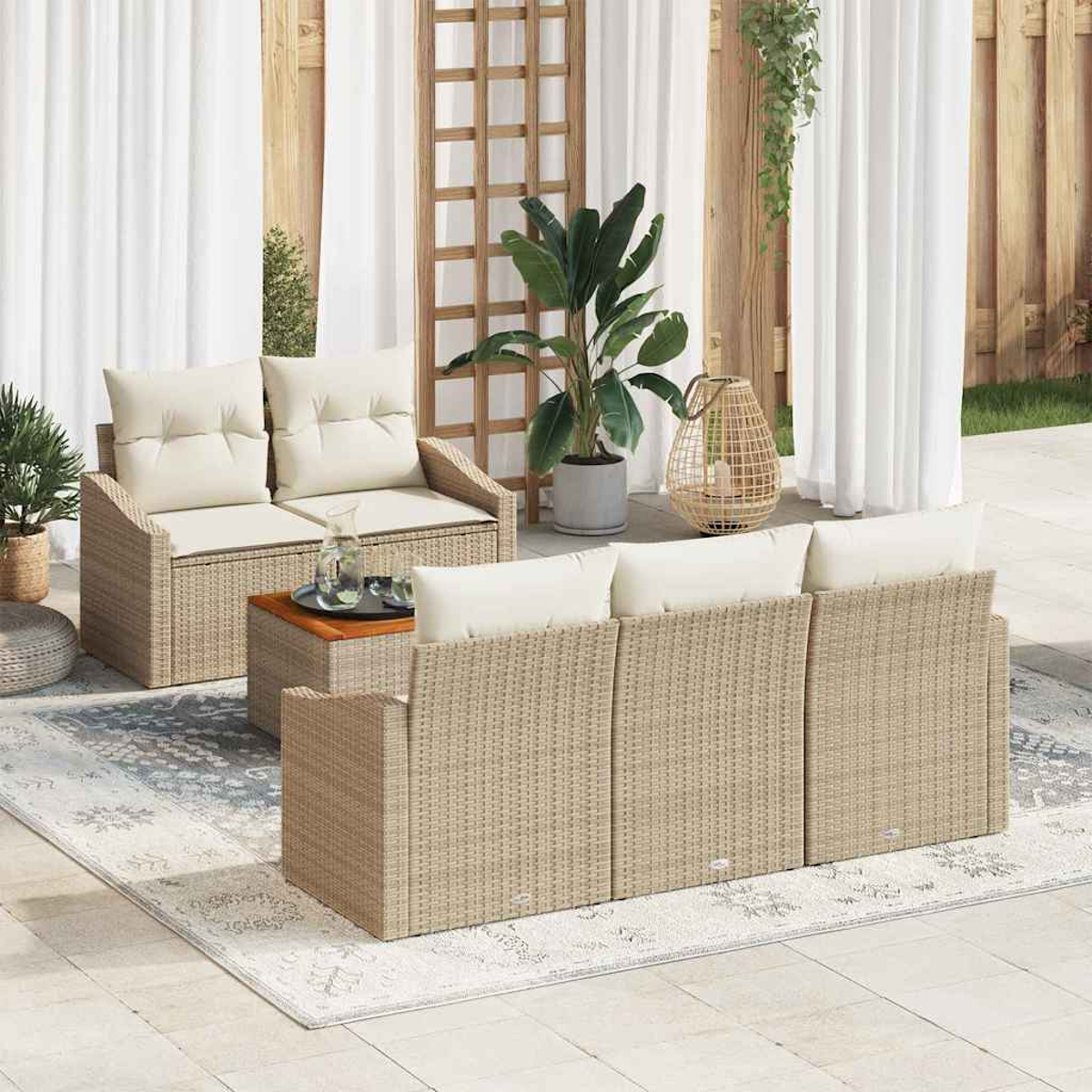 Terrassenset mit beigefarbenen Korbsitzmöbeln und Kissen. Enthält einen Couchtisch und Pflanzen, auf einem gemusterten Teppich. Weiße Vorhänge im Hintergrund.