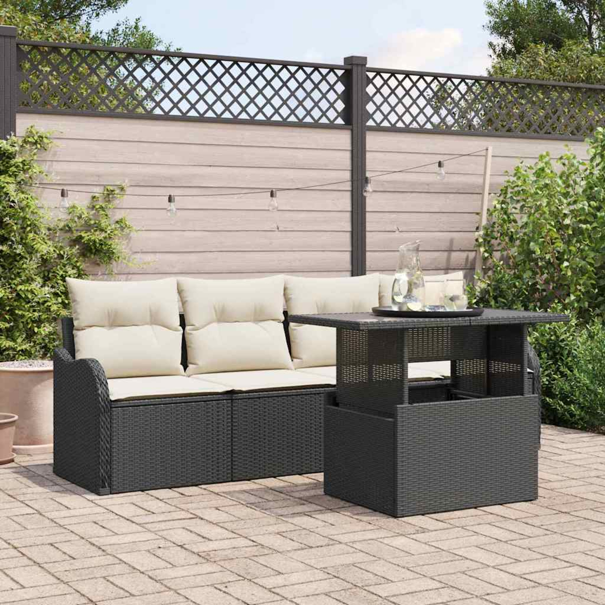 Garten-Terrassenset mit einem schwarzen Korbmöbel-Sofa und -Tisch. Beige Kissen und ein Holzzaun im Hintergrund. Lichterketten sind an.