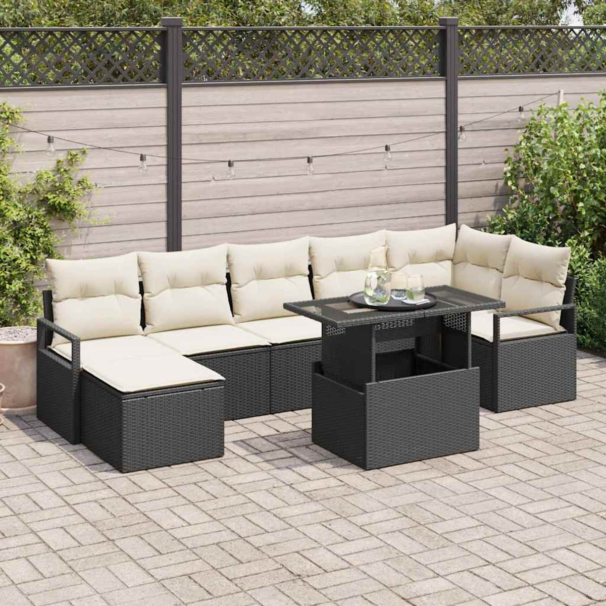 Outdoor-Terrassenset mit beigefarbenen Kissen und einem schwarzen Tisch auf einer gepflasterten Terrasse. Ein Holzzaun und Grünzeug im Hintergrund.