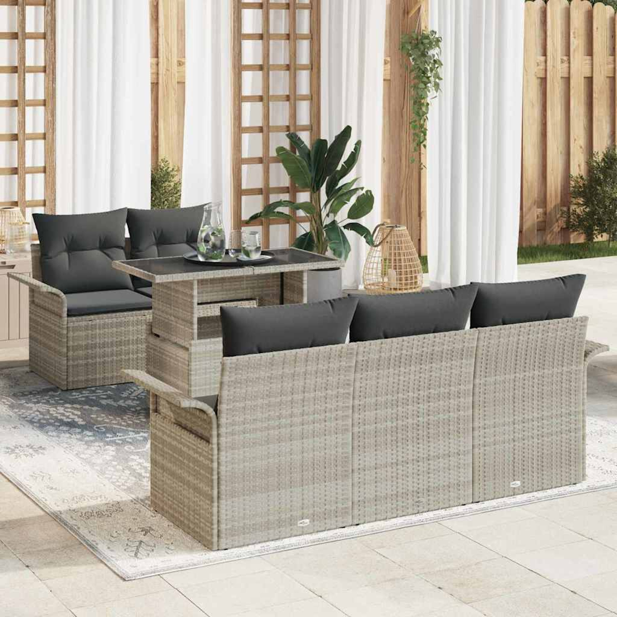 Garten-Rattanmöbel-Set mit grauen Kissen und einem Tisch. Im Hintergrund Vorhänge und ein Holzzaun.