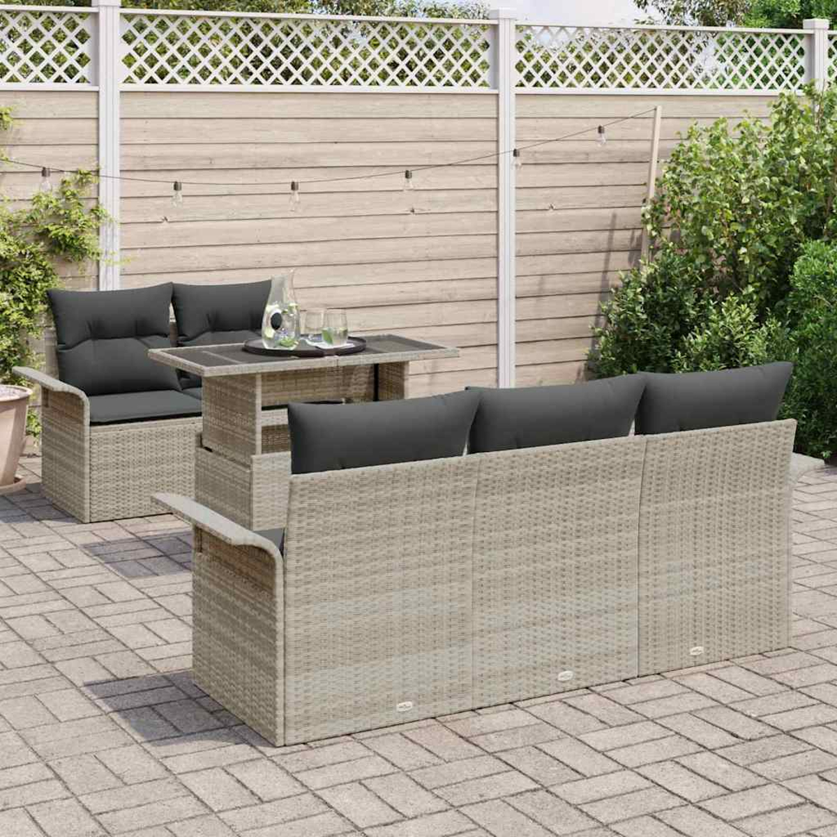 Terrassenset mit grauen Kissen und einem Tisch. Vor einem Zaun und etwas Grün. Der Boden besteht aus Ziegeln.