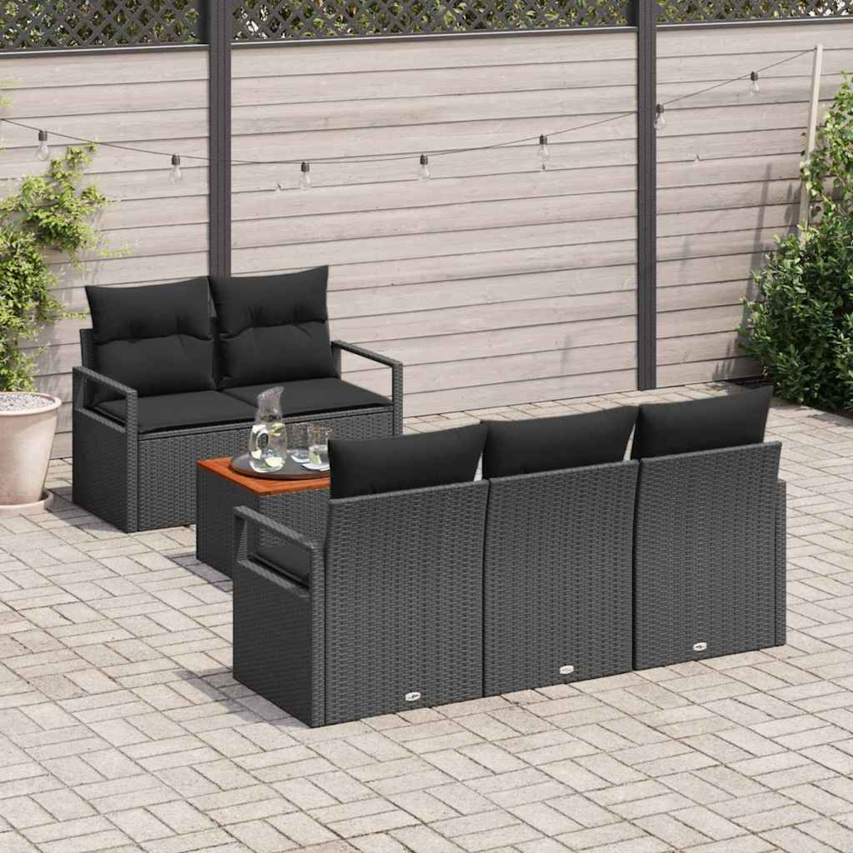 Terrassenset mit grauen Korbmöbeln und schwarzen Kissen. Enthält eine Liebescouch, ein Sofa und einen kleinen Holztisch. Steinpflasterung.